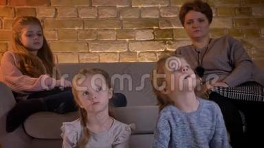 在舒适的家中，白种人的母亲和三个女儿坐在一起专心看电影的特写镜头